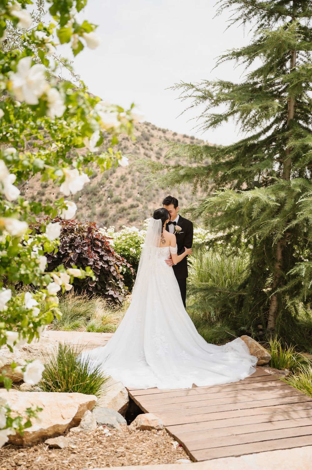 A bride and groom are kissing on a wooden bridge.