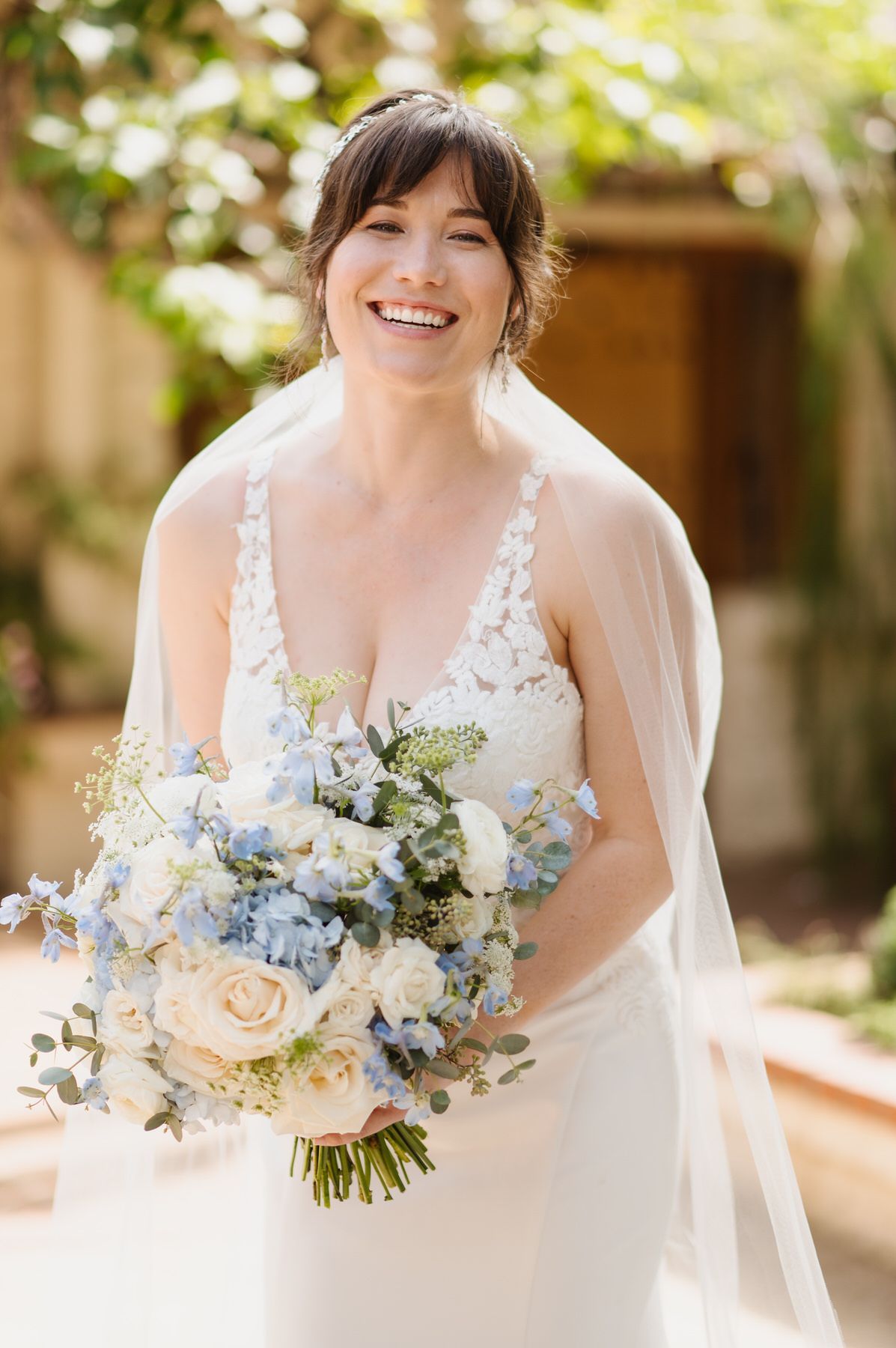 A bride in a white dress and veil is holding a bouquet of blue and white flowers.