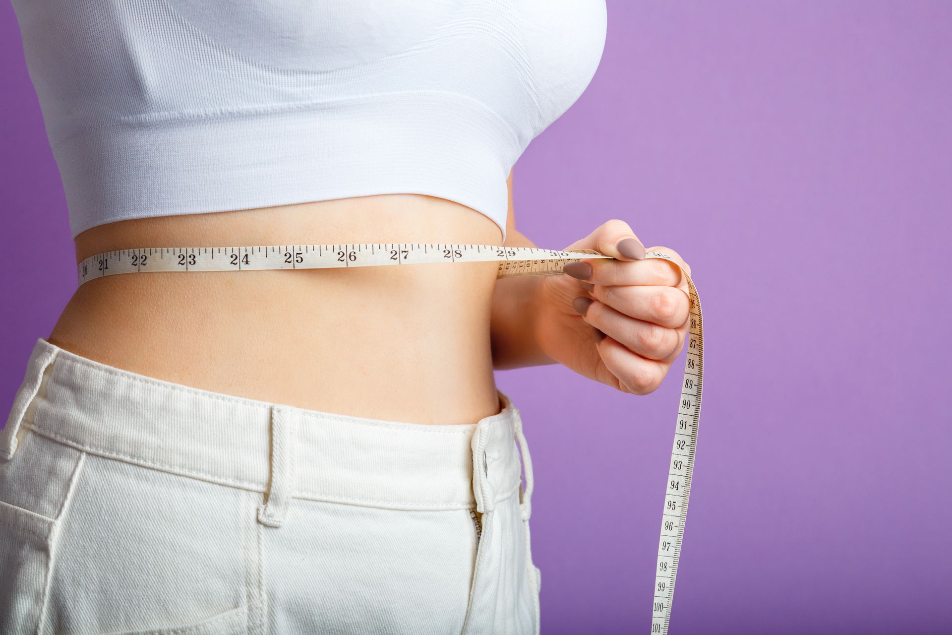 A woman is measuring her waist with a tape measure.