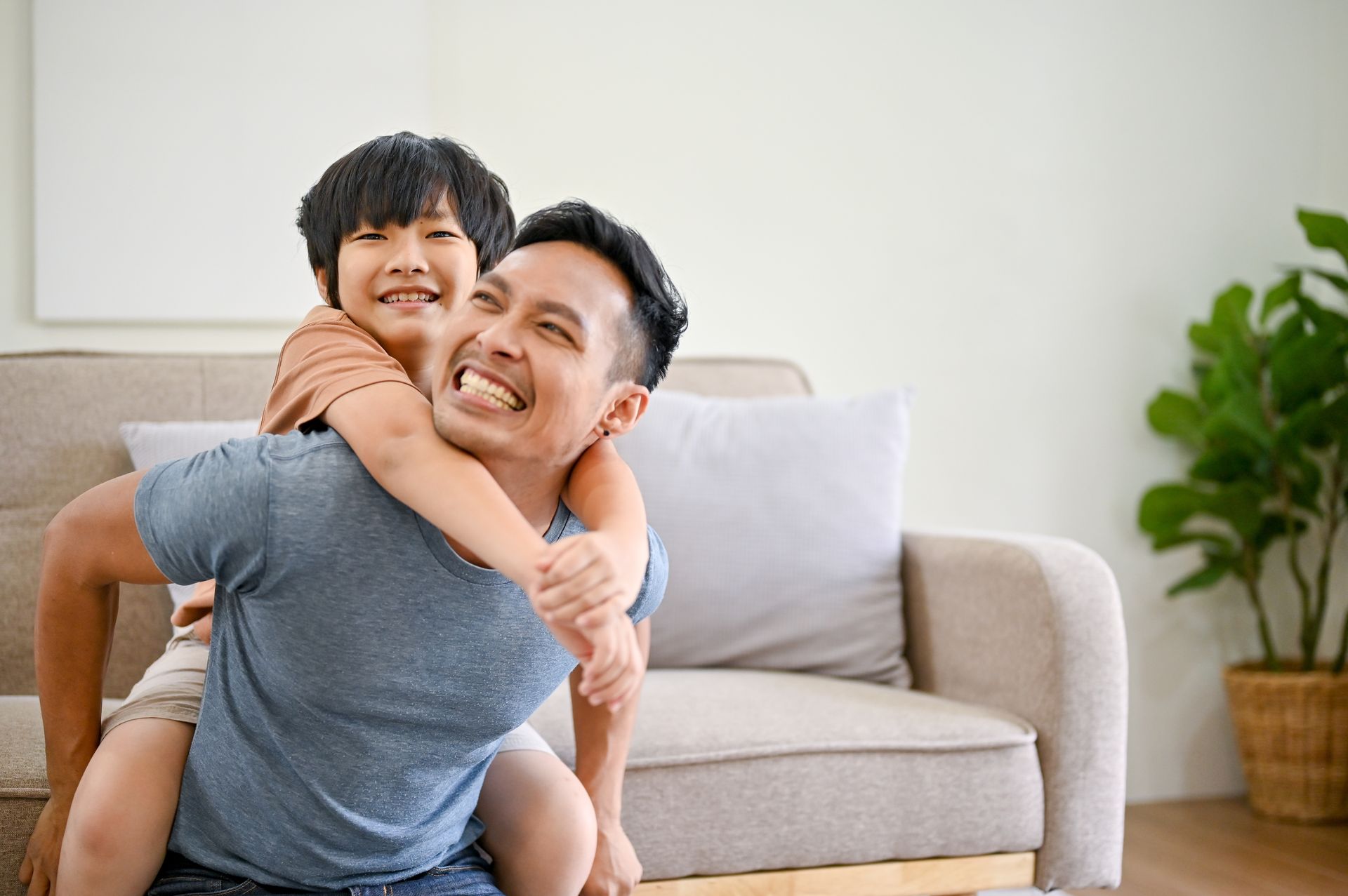 Asian father giving piggyback ride to smiling son at home.