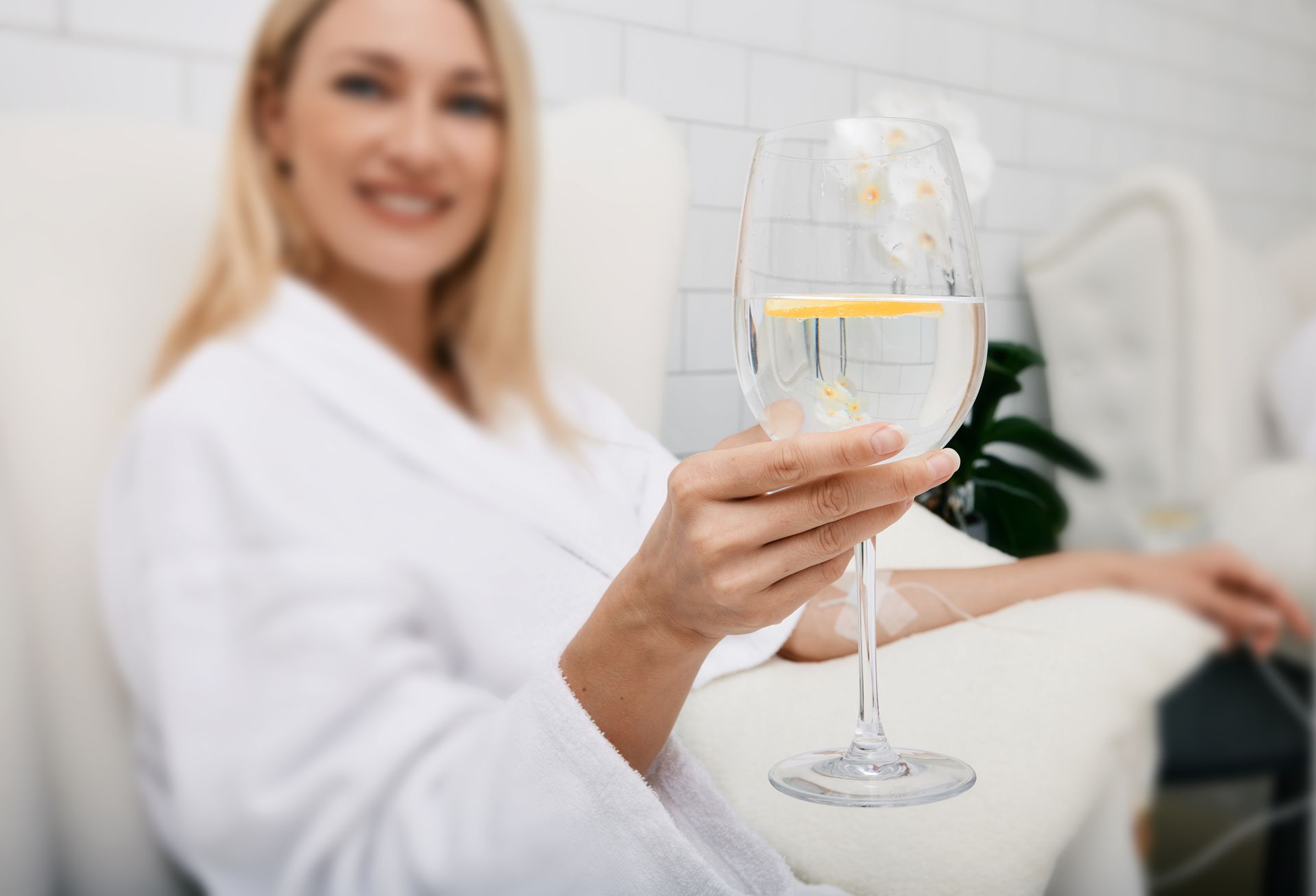 Happy woman in spa robe holding a glass of lemon water, enjoying hydration