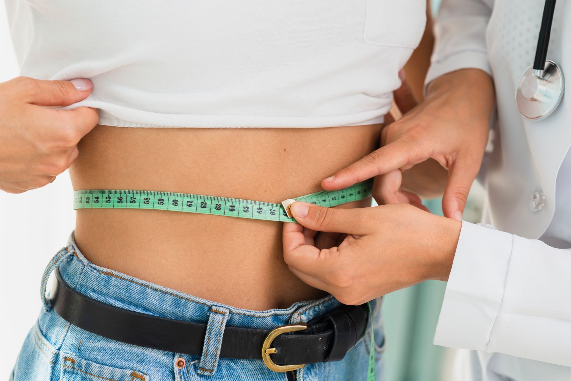 A doctor is measuring a woman 's waist with a tape measure.