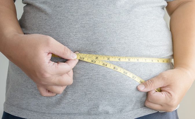 A person is measuring their waist with a tape measure.