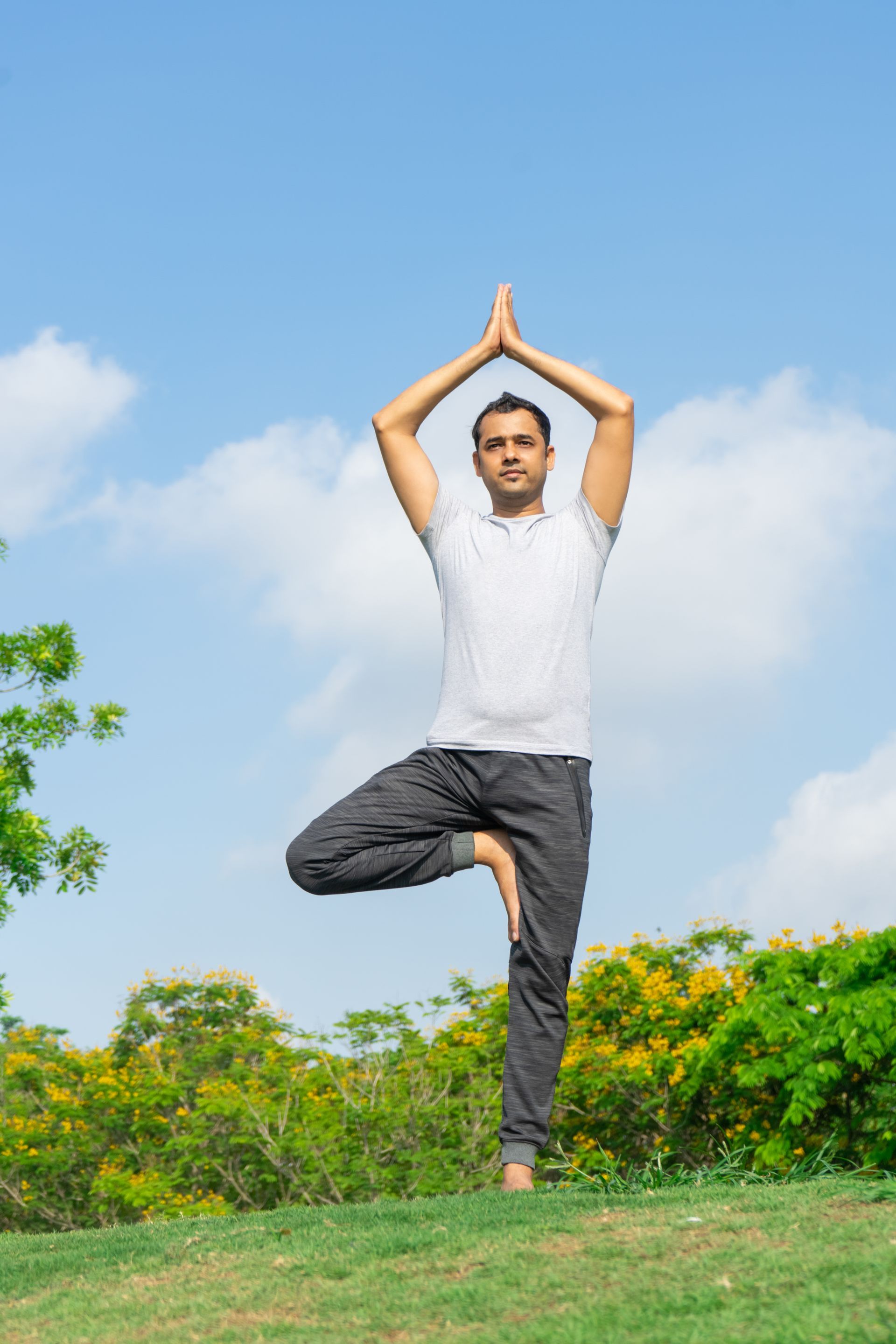 A man is standing on one leg in a tree pose in a park.