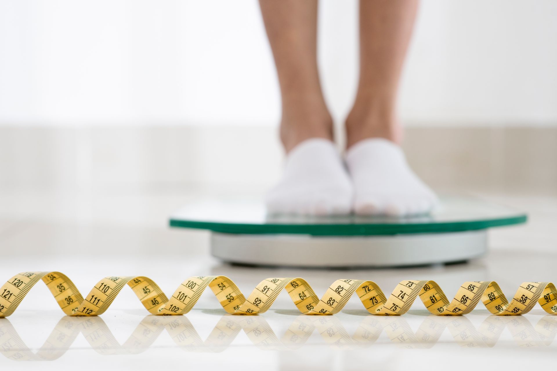 A woman is standing on a scale next to a measuring tape.