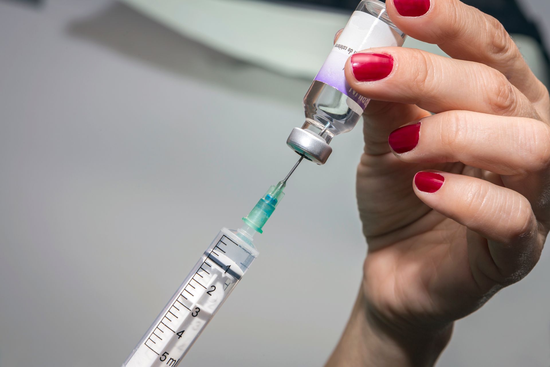 A woman with red nails is holding a syringe and a bottle of vaccine.