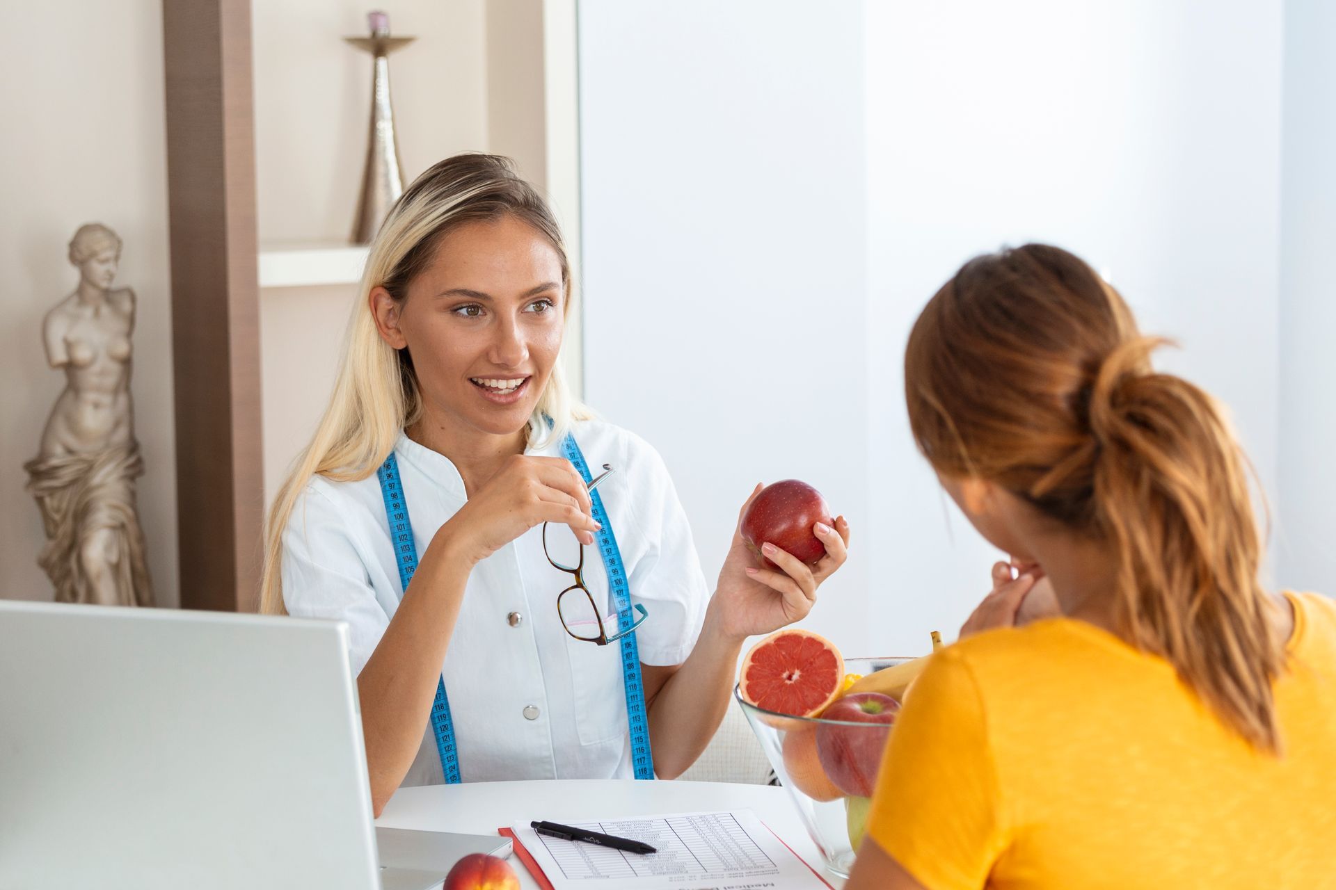 A woman is sitting at a table talking to a nutritionist who is holding an apple.