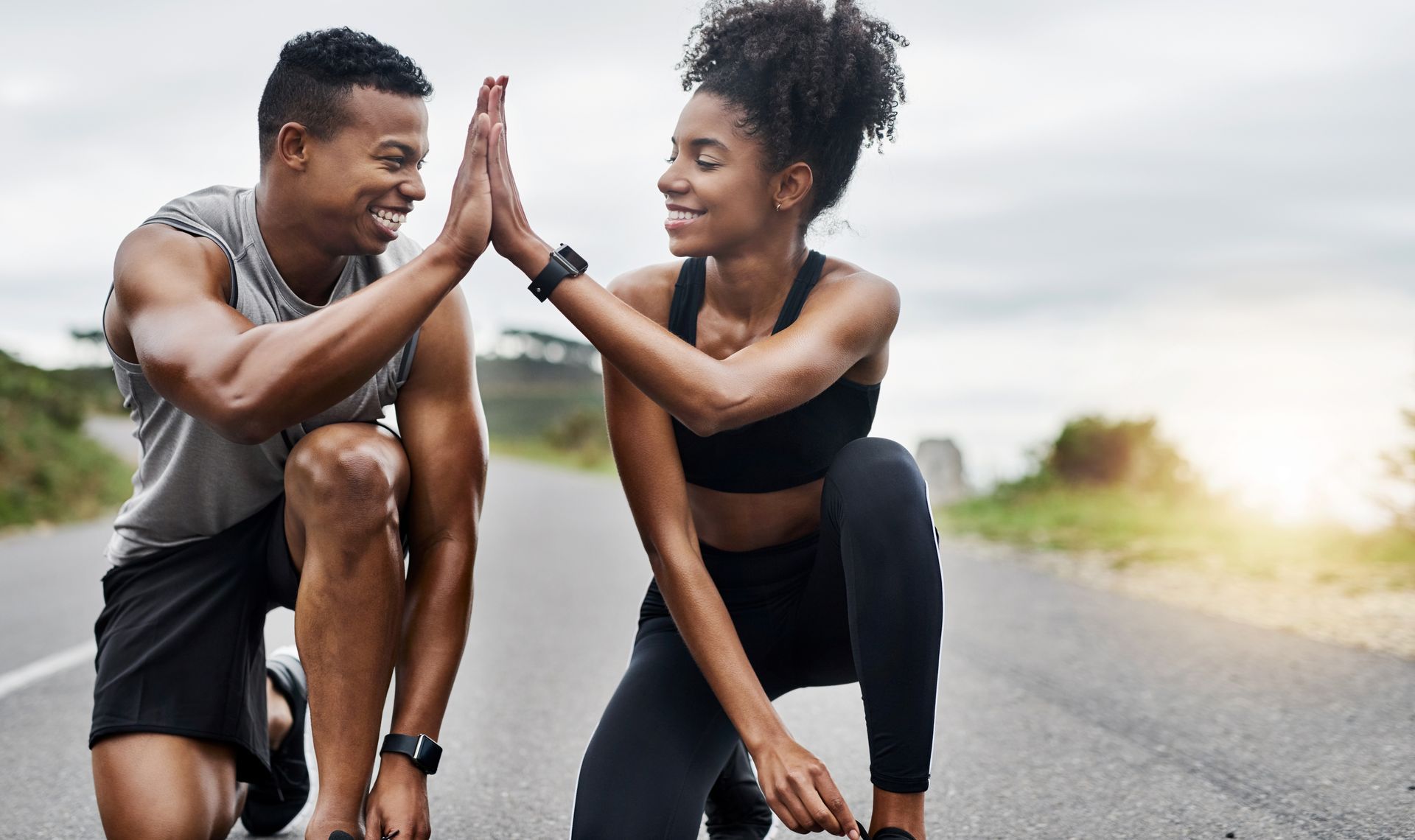 Two athletes high-fiving after a run on an open road, smiles, fitness tracker.