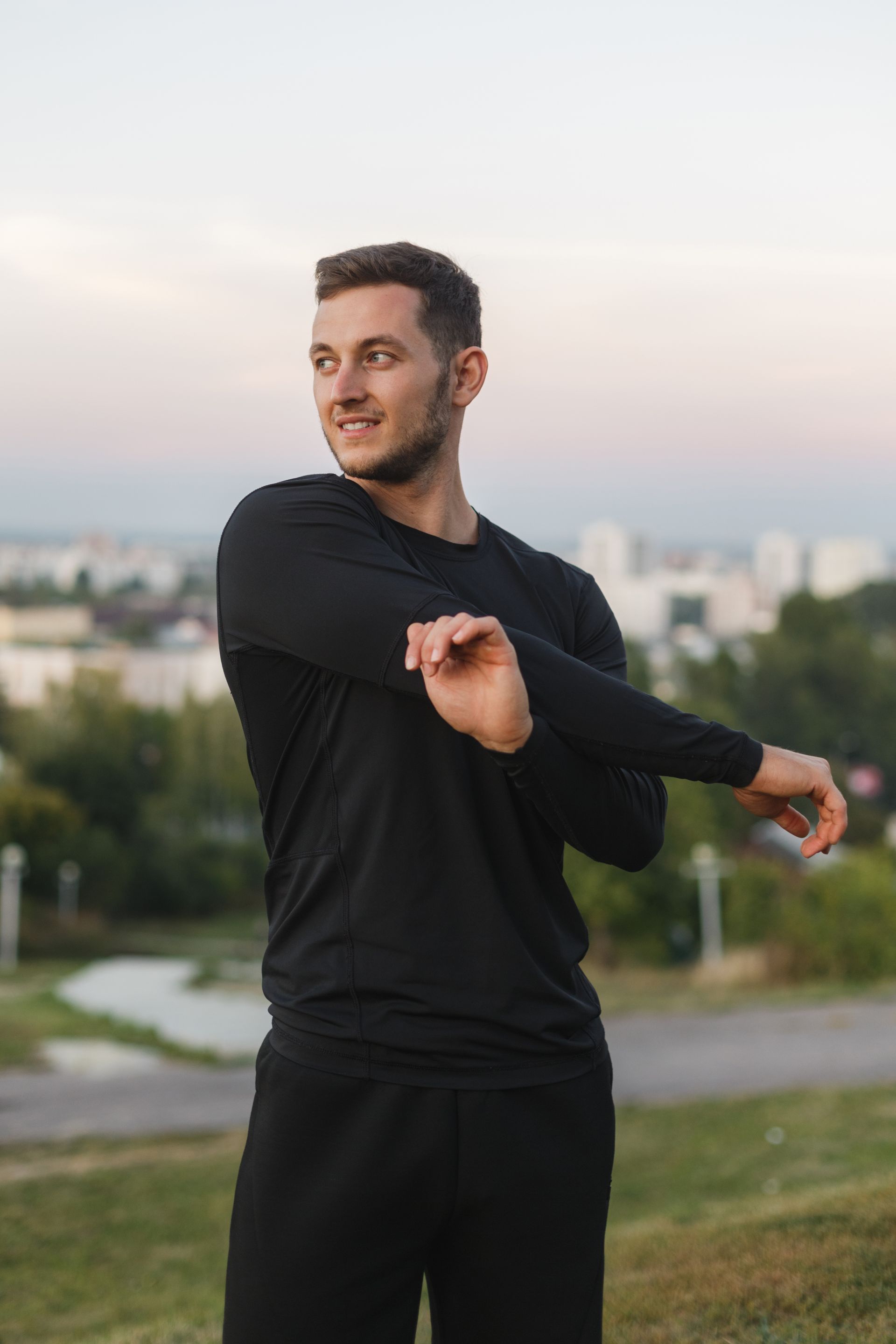 A man in a black shirt is stretching his arms in a park.