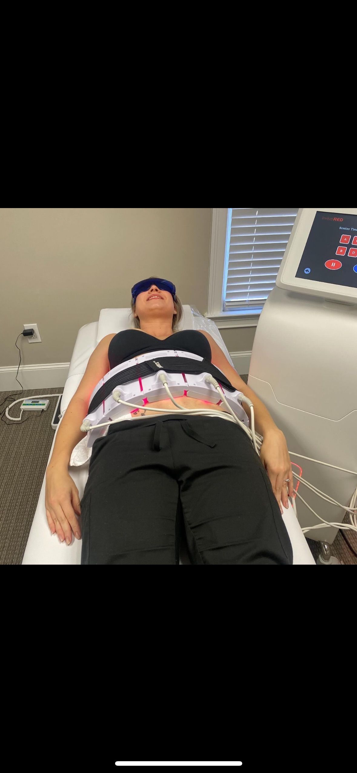 A woman is laying on a bed with a machine on her stomach.