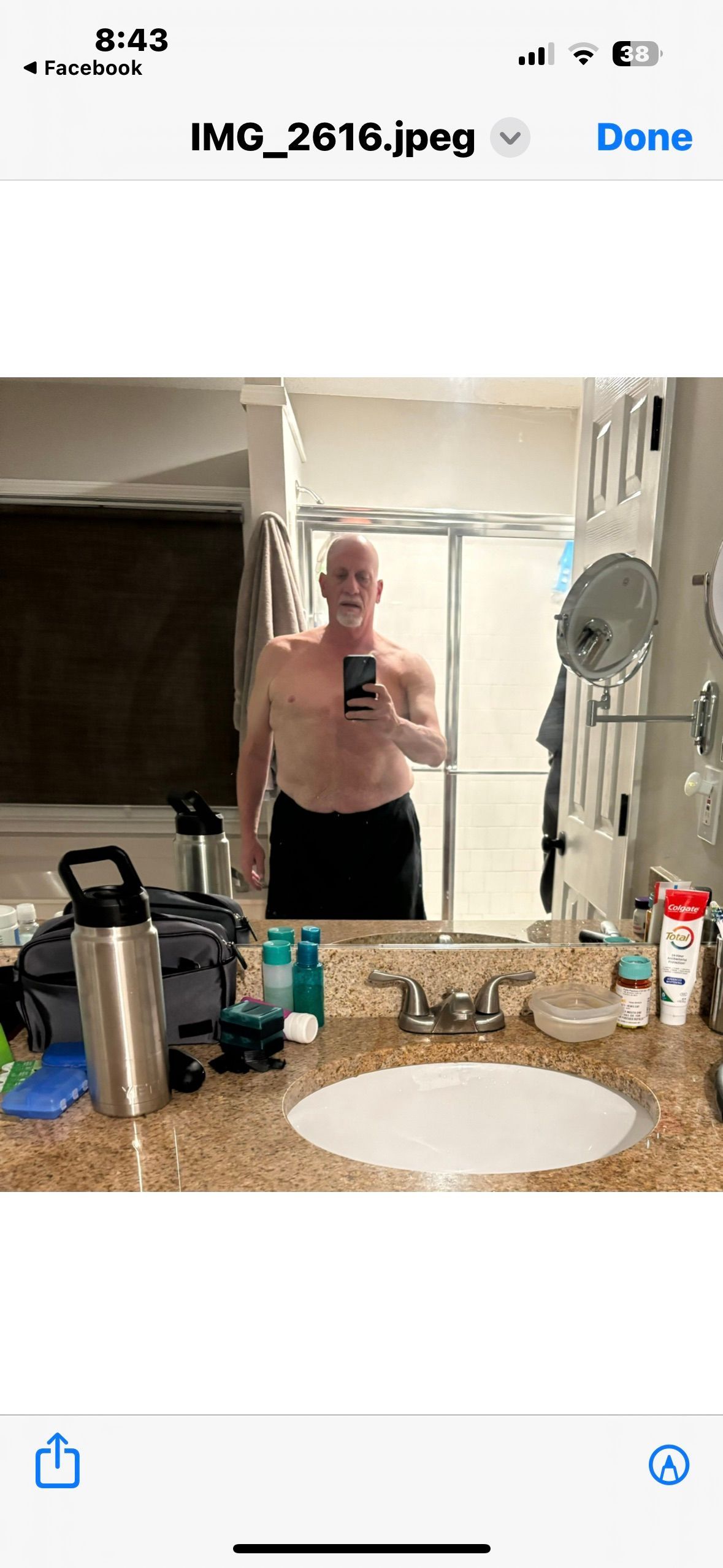 A shirtless man is taking a selfie in a bathroom mirror.