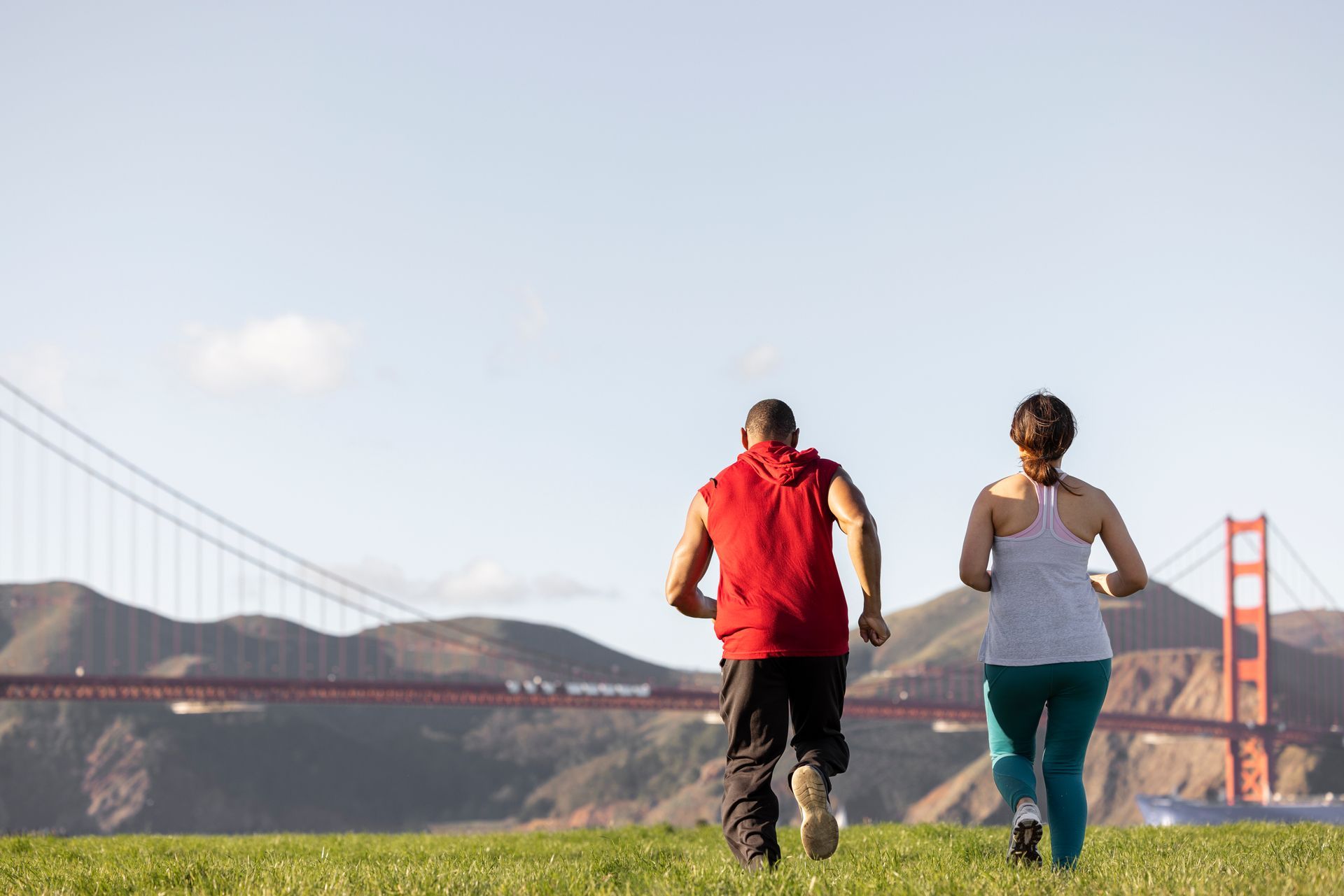 A man and a woman are running in front of the golden gate bridge.