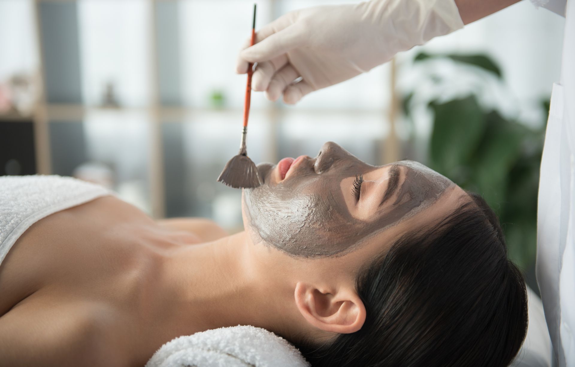 A woman is getting a charcoal mask on her face at a spa.