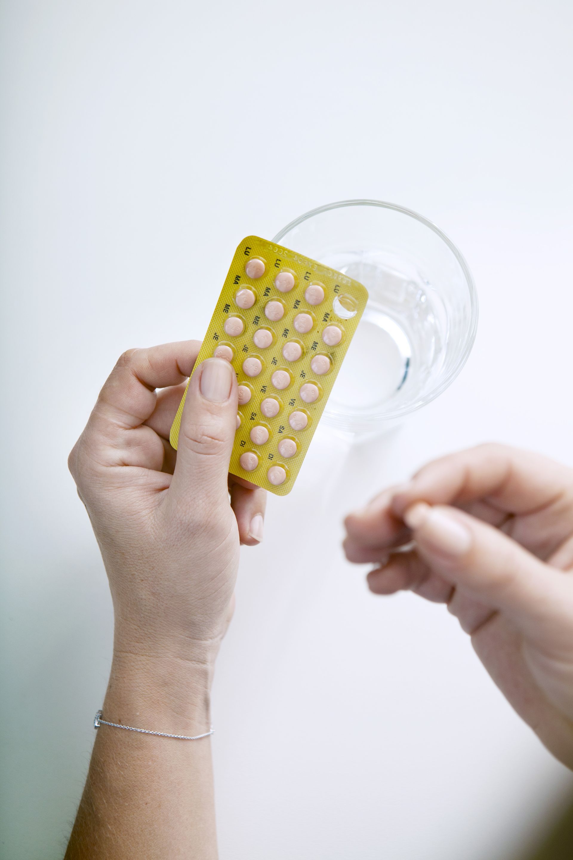 A woman is holding a blister pack of pills and a glass of water.