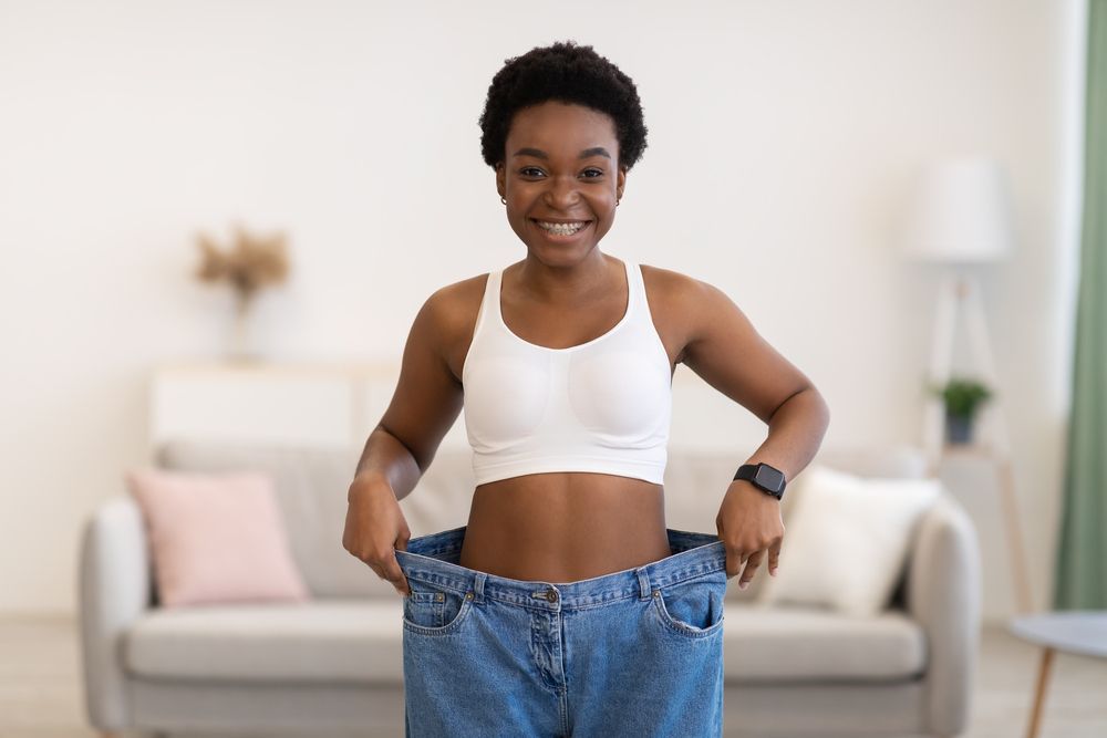 A woman is standing in a living room wearing a pair of oversized jeans.