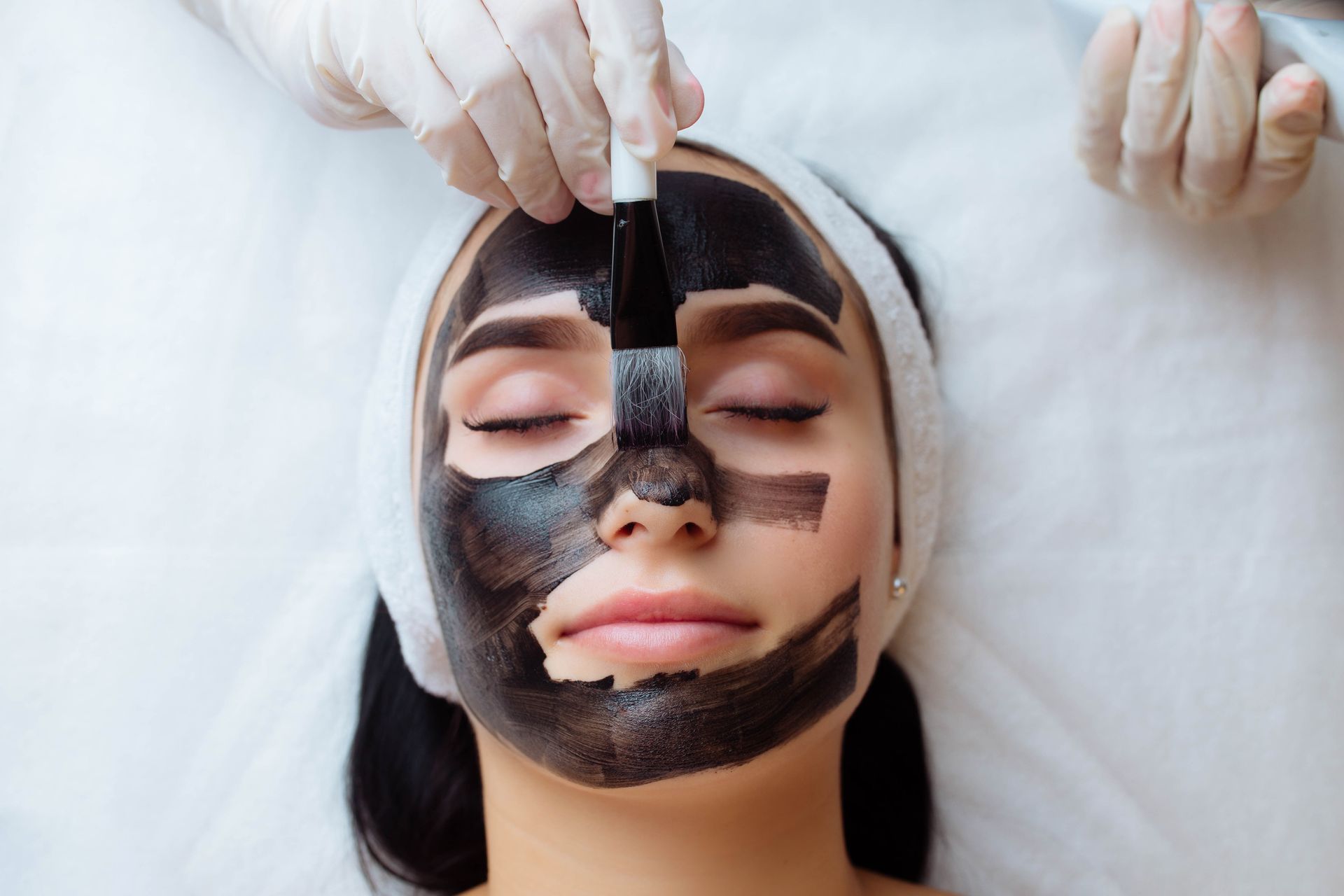 A woman is getting a charcoal mask on her face.