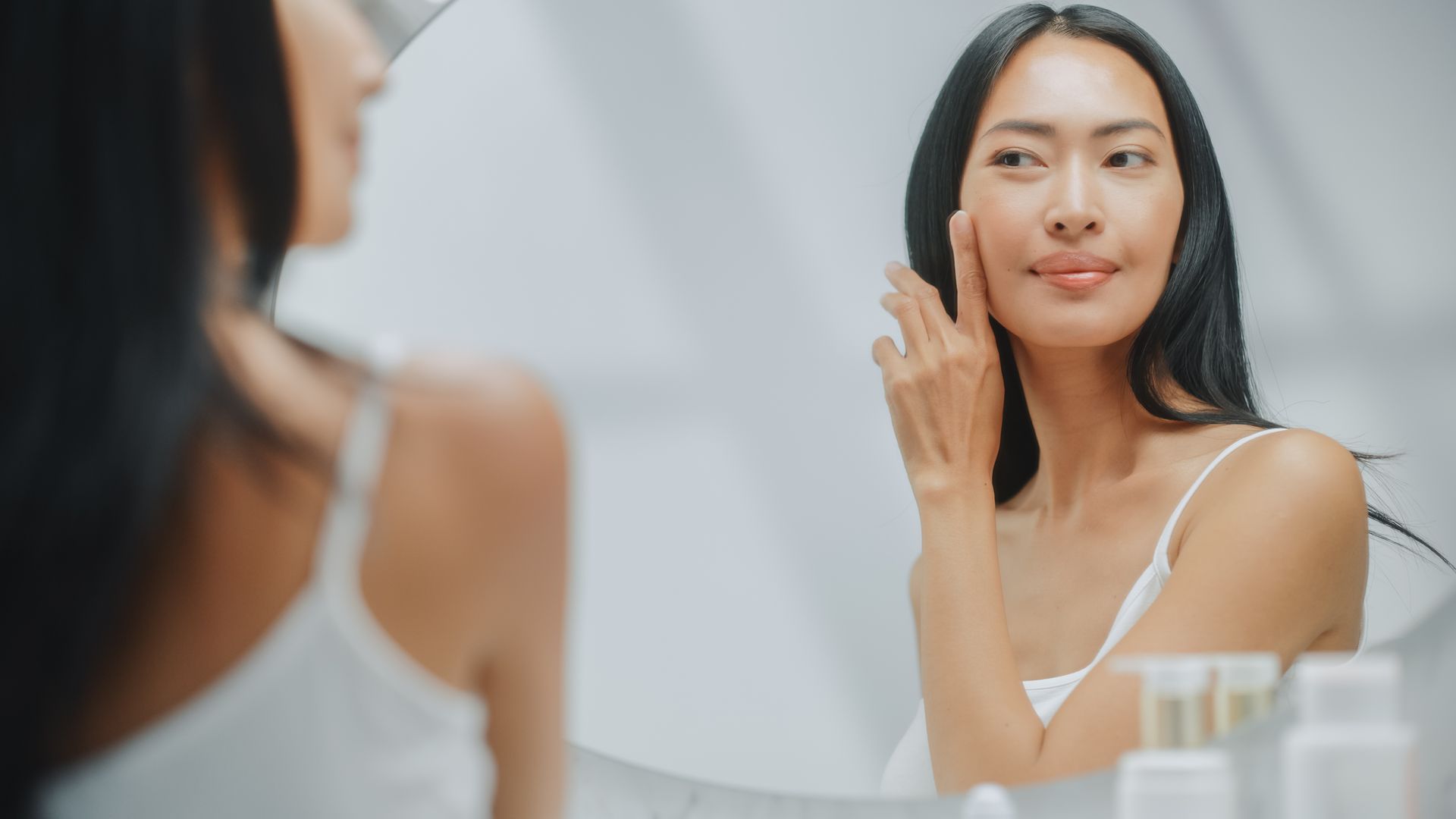 A woman is looking at her face in the mirror.