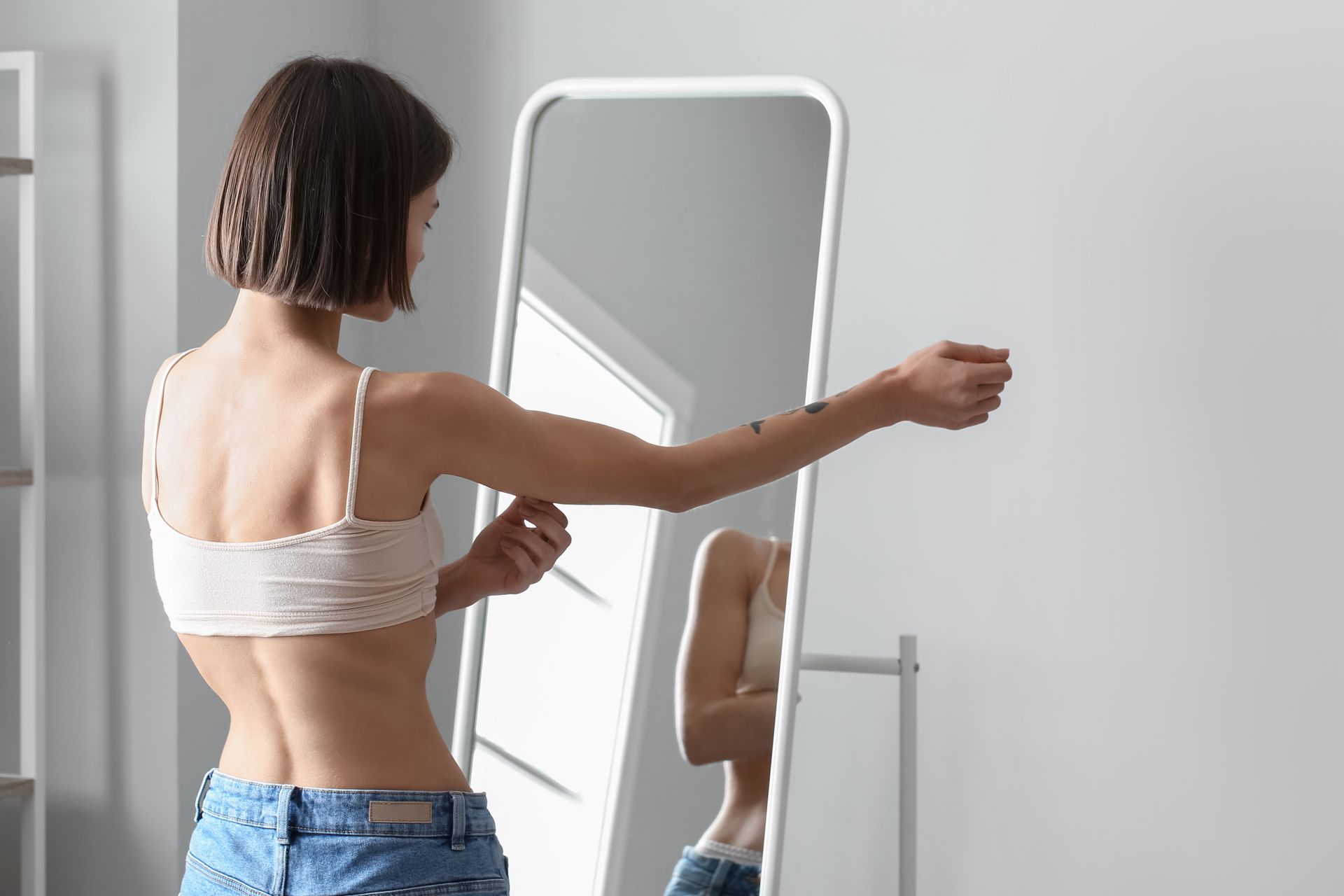 A woman is looking at her reflection in a full length mirror.