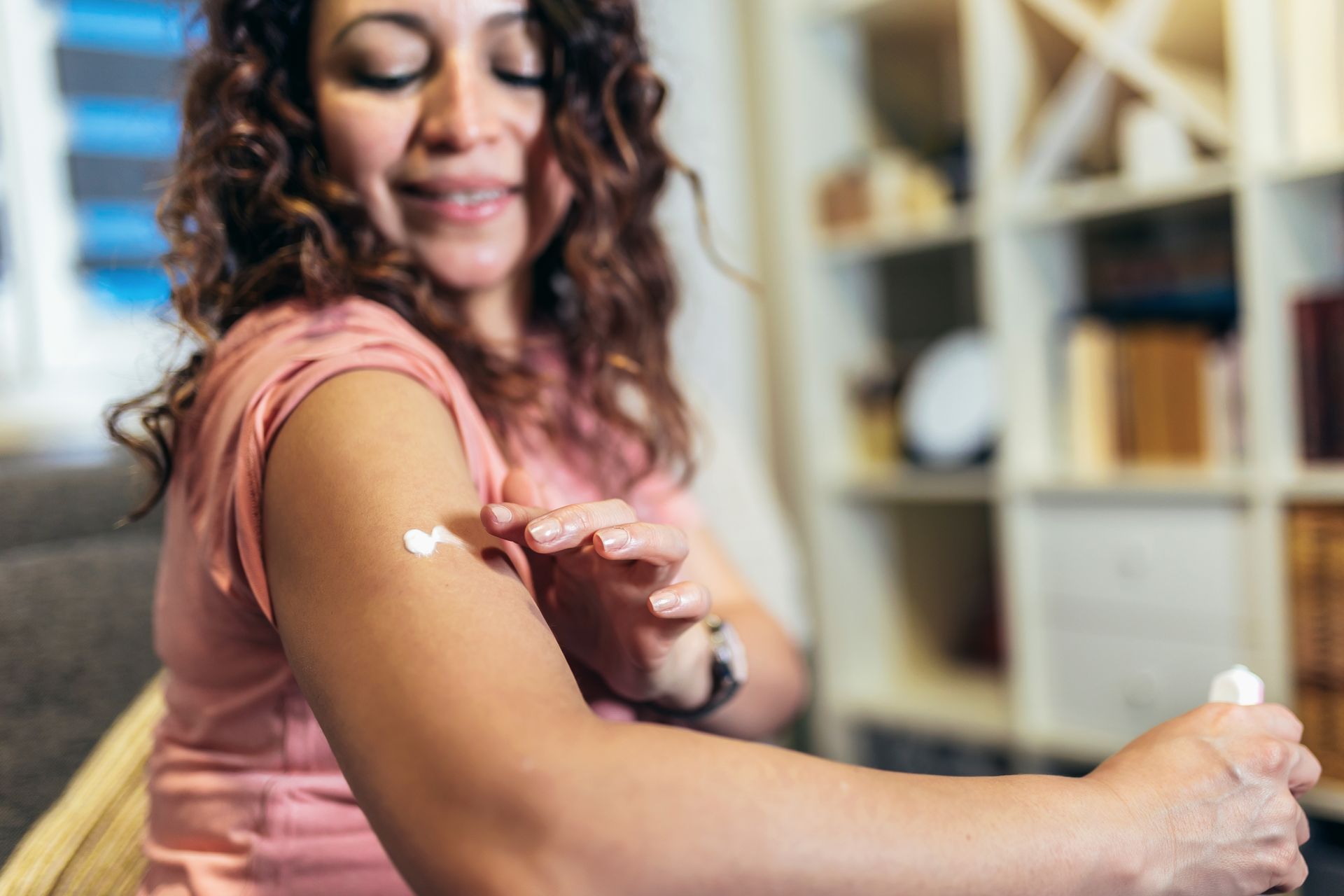 A woman is applying lotion to her arm while sitting on a couch.