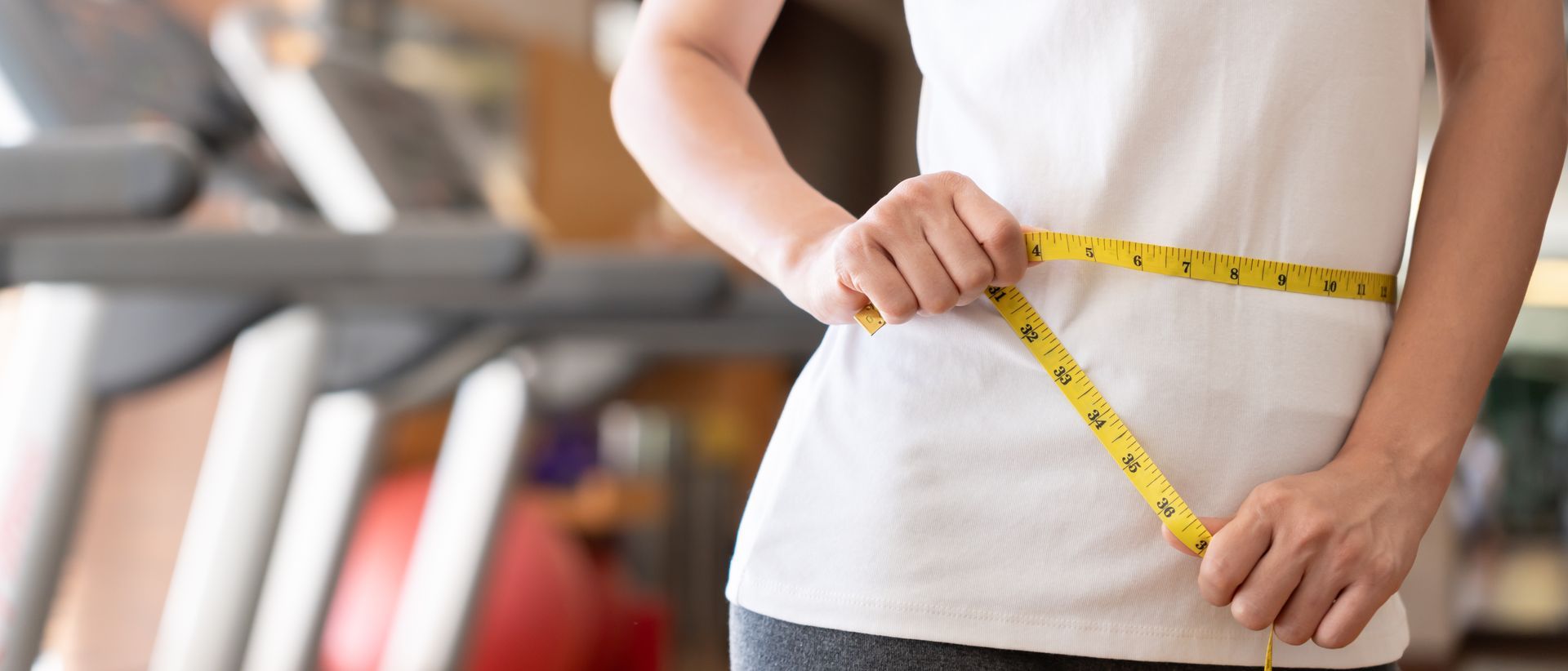 A woman is measuring her waist with a tape measure in a gym.