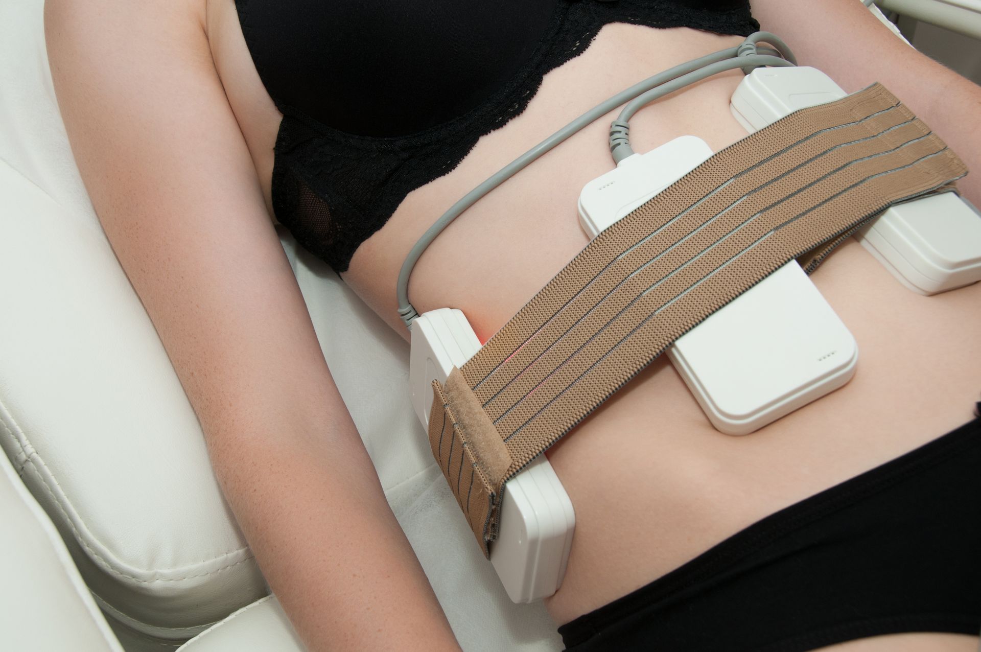 A woman is laying on a bed with a belt around her stomach.