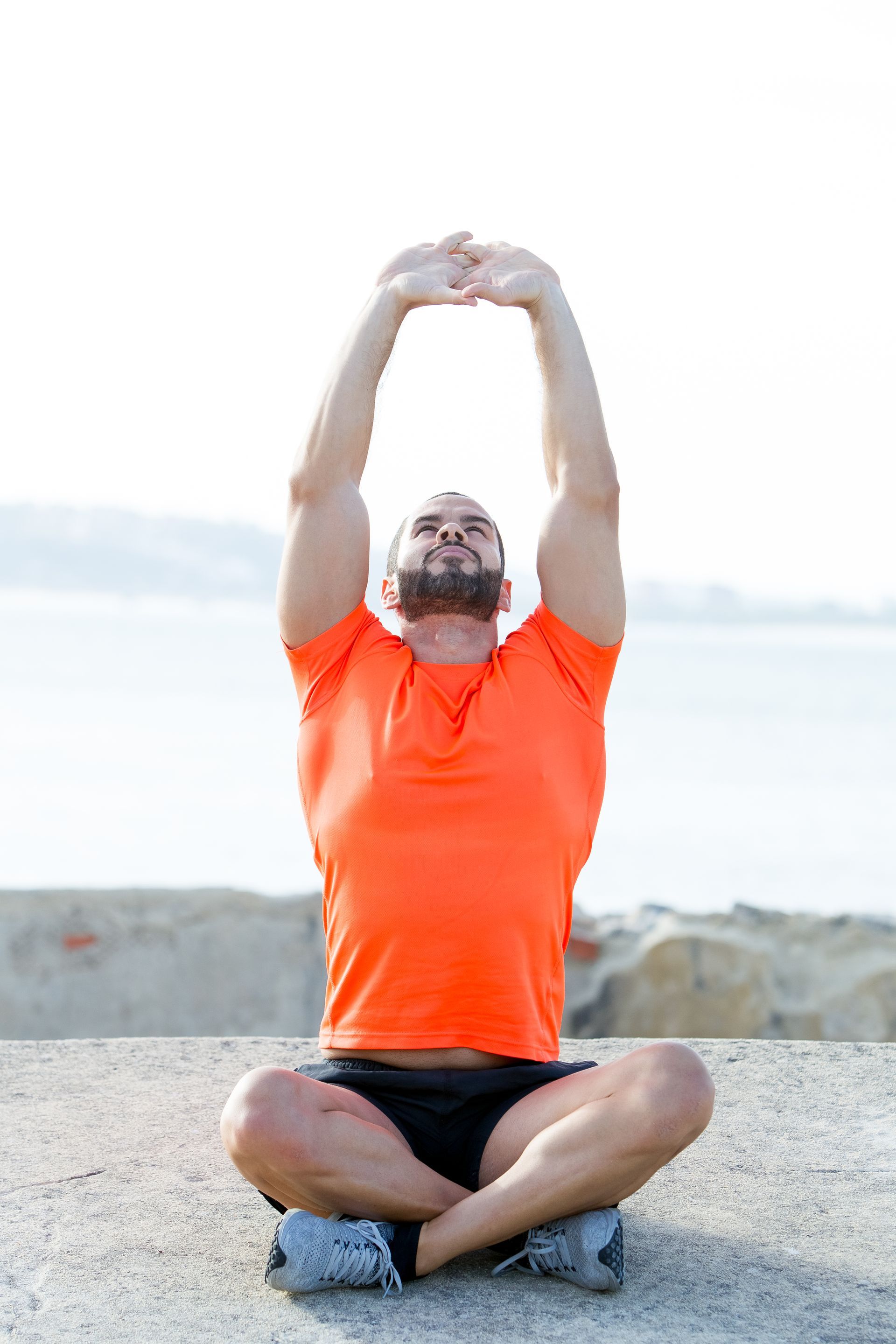 A man is sitting on the ground with his legs crossed and his arms up.