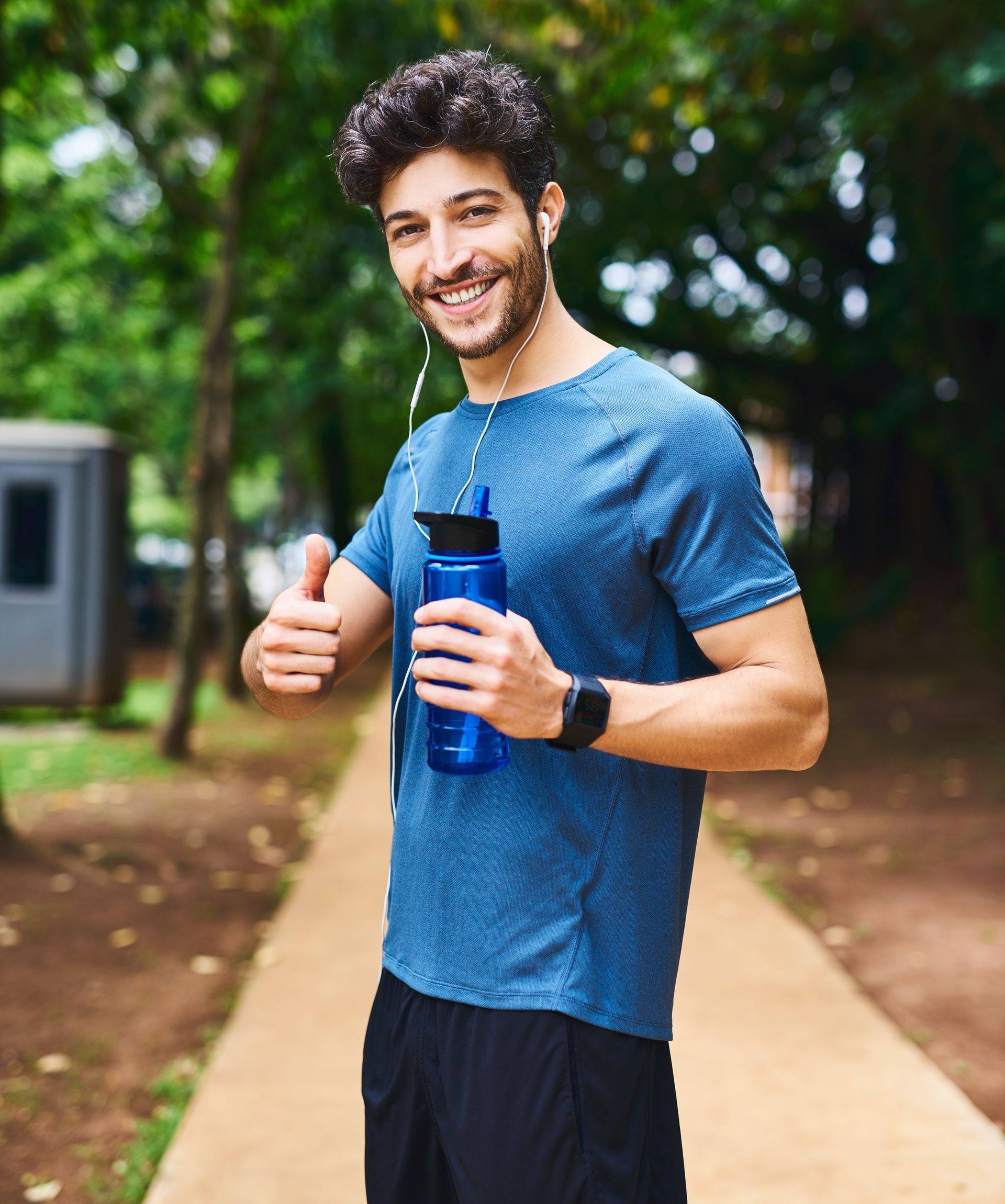 A man is holding a blue water bottle and giving a thumbs up.