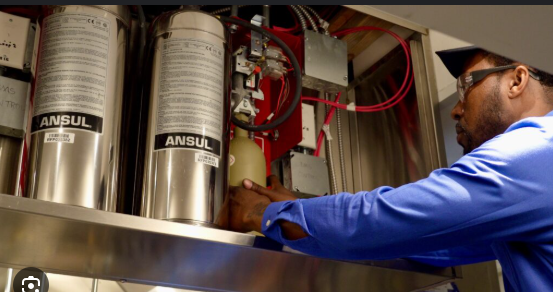 Person in a safety vest holds clipboard, pen, indoors.