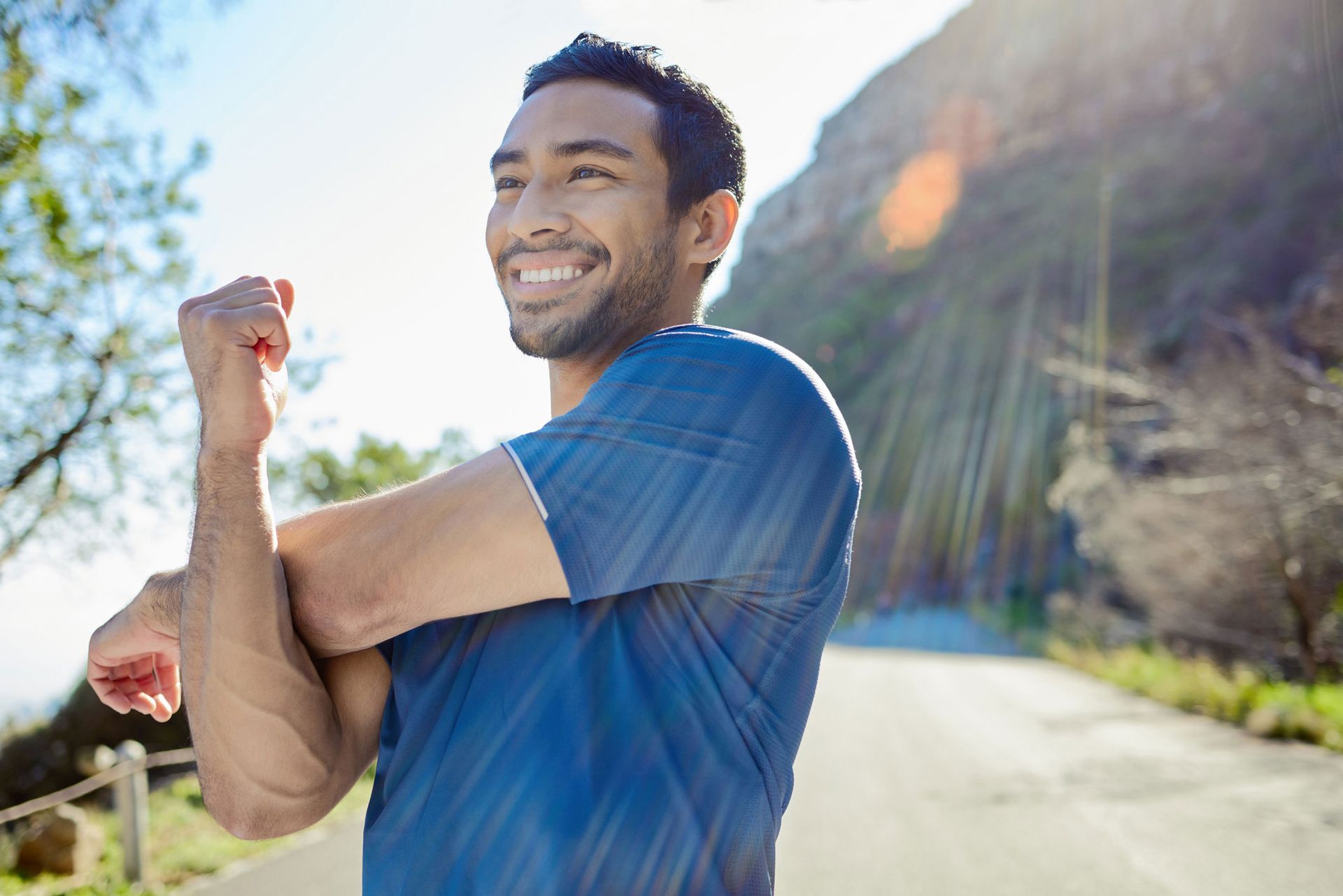 A man is stretching his arms while standing on a road.