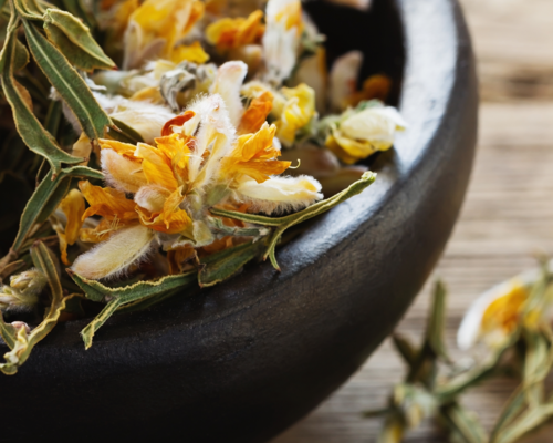 A black bowl filled with dried flowers and leaves on a wooden table.