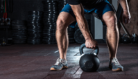 A man is lifting a kettlebell in a gym.