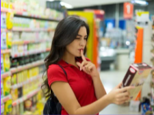 A woman is holding her finger to her lips while looking at a box in a store.