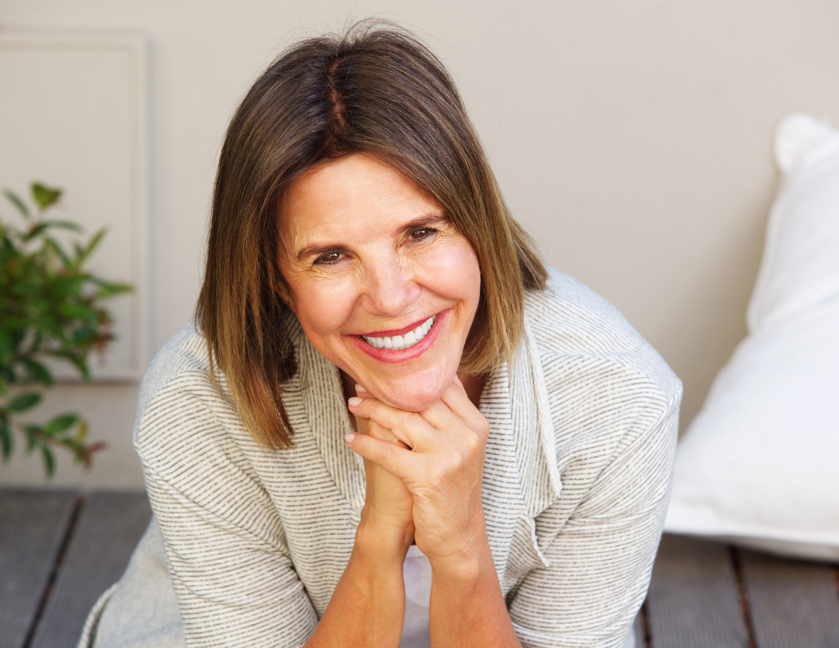 A woman is sitting on the floor with her hands on her chin and smiling.