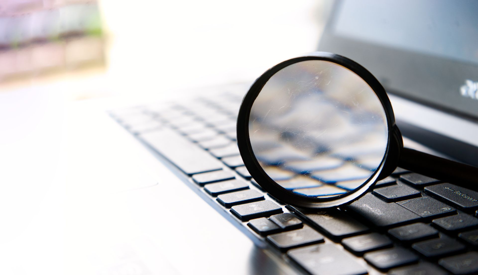 Magnifying glass on laptop keyboard, suggesting close inspection or searching