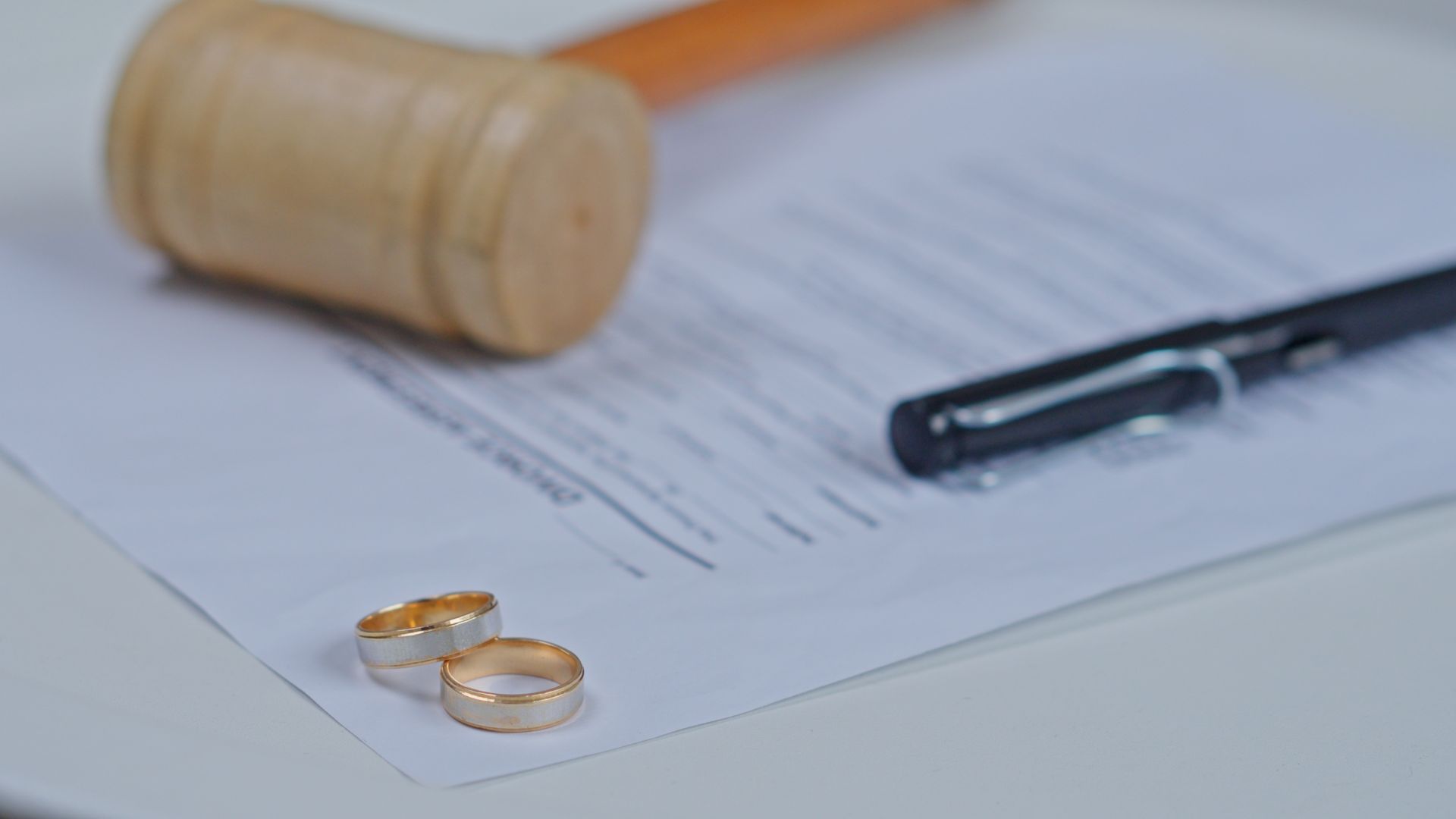 Wedding rings, pen, and document with gavel on a desk.