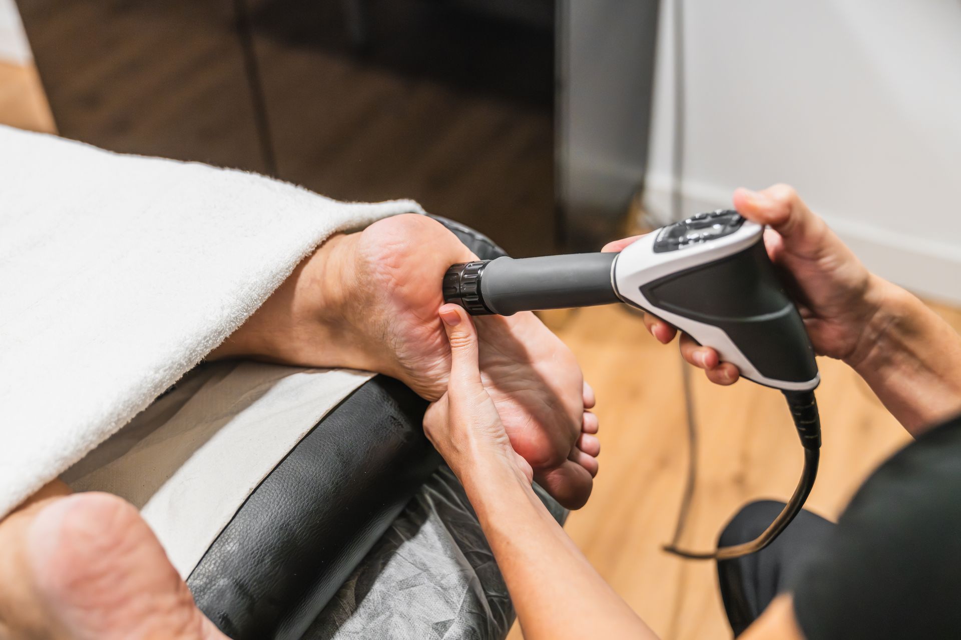 Handheld massage gun applied to a person's wrist during a physical therapy session.