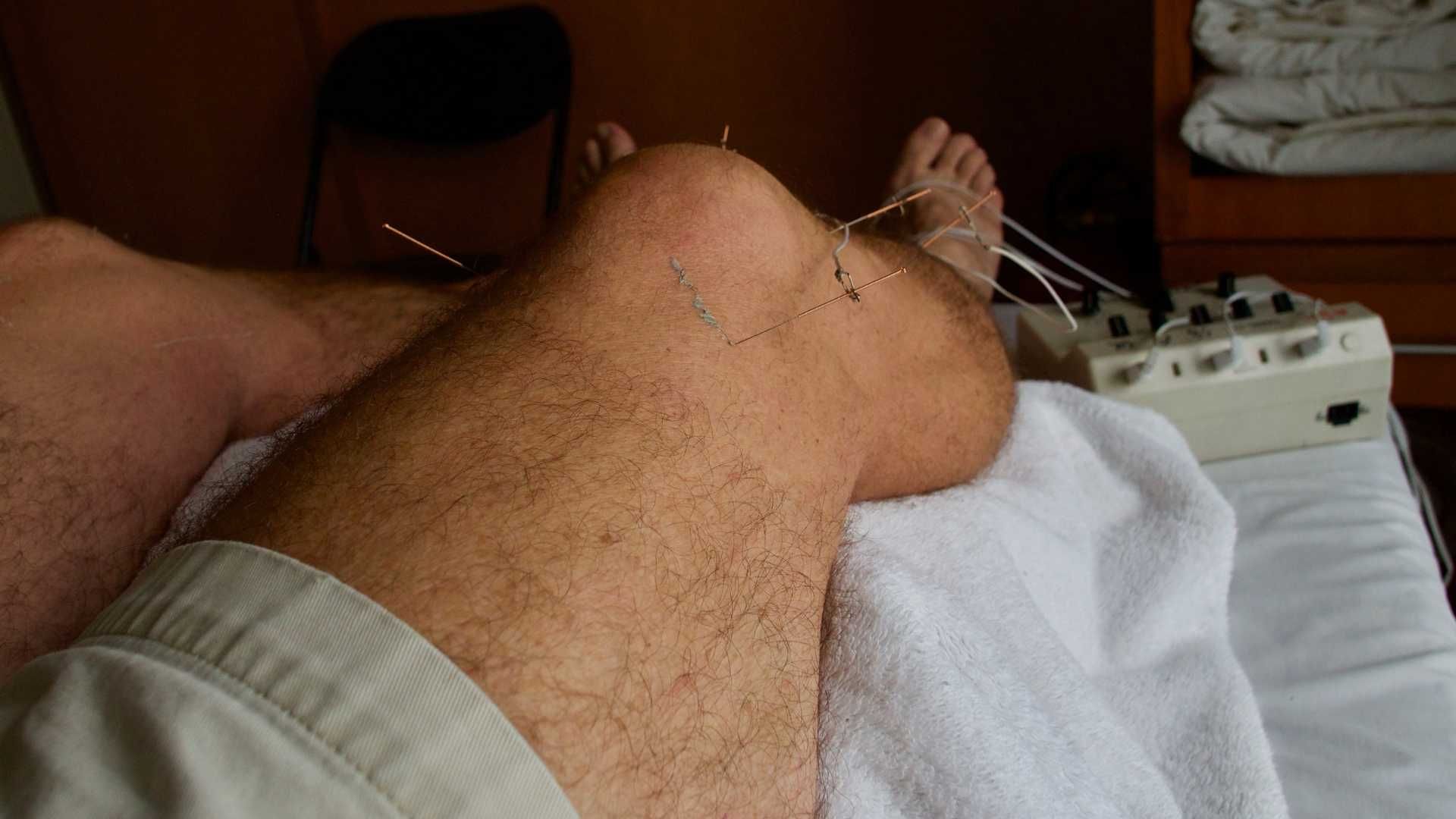 Legs resting on a bed with a white towel and a medical device near the feet