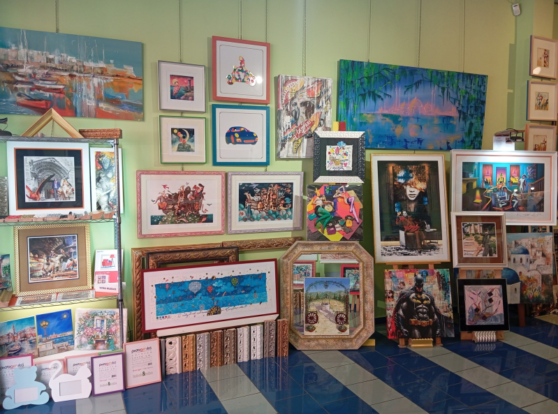 Una galleria d'arte con numerosi dipinti incorniciati di varie dimensioni e stili esposti sulle pareti e sul pavimento.