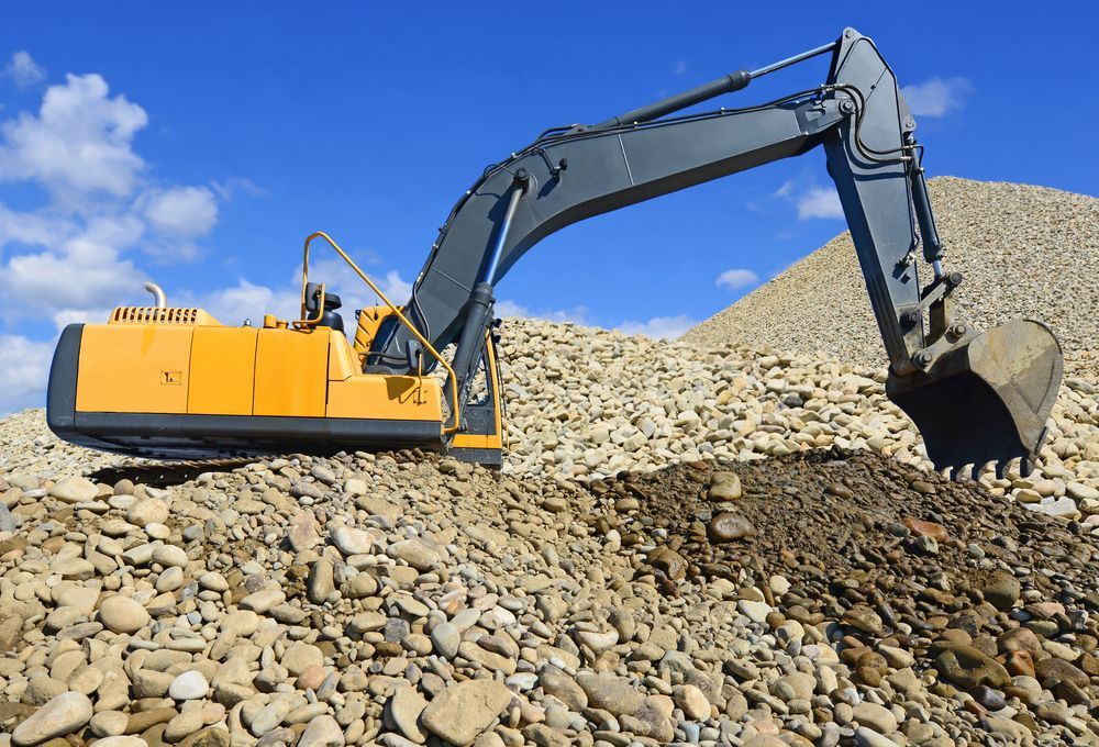 Yellow Excavator Digging in a Pile of Rocks Under a Blue Sky — B&T Earthworks & Civil in Yorkeys Knob, QLD