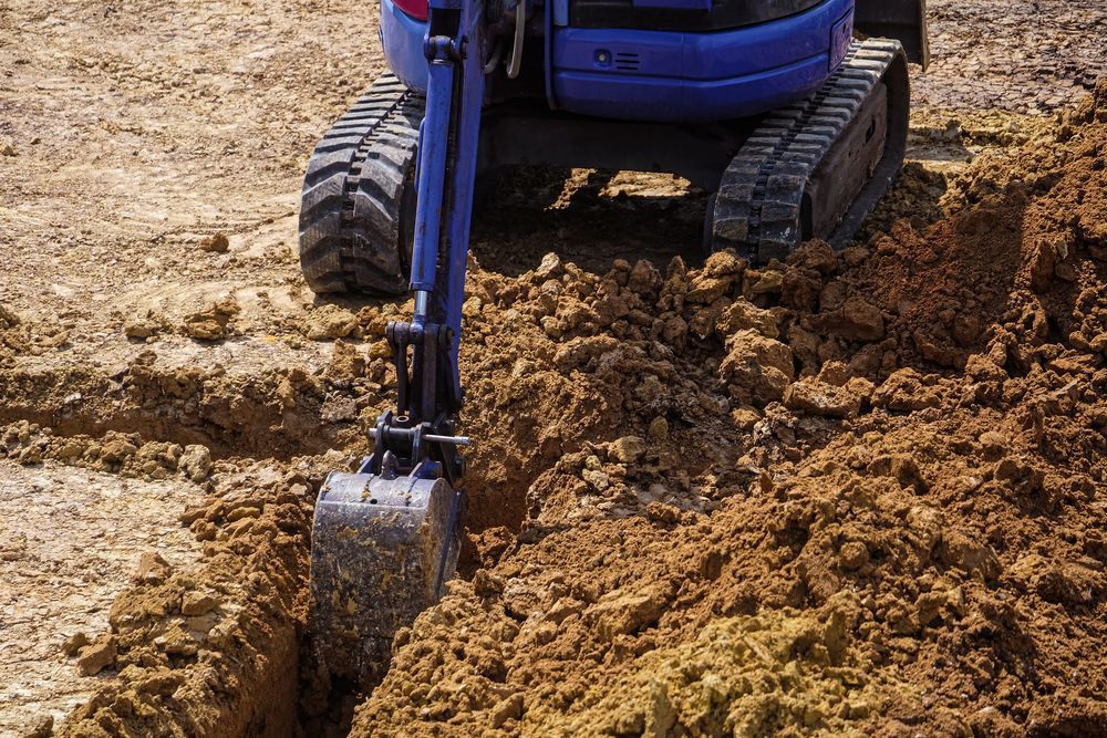 Small Blue Excavator Digging a Trench in Brown Dirt — B&T Earthworks & Civil in Yorkeys Knob, QLD