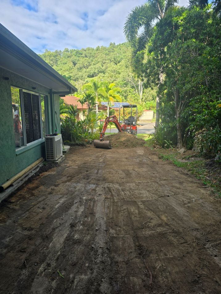A Small Excavator Digging in a Dirt Yard Next to a Green House — B&T Earthworks & Civil in Yorkeys Knob, QLD