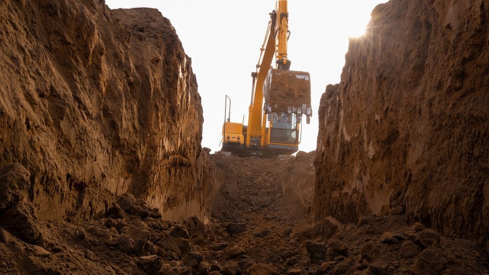 An Excavator Digging a Trench in Brown Earth, Bright Sunlight Behind — B&T Earthworks & Civil in Yorkeys Knob, QLD