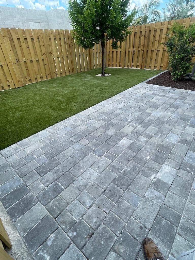 A patio with a wooden fence and a tree in the backyard.