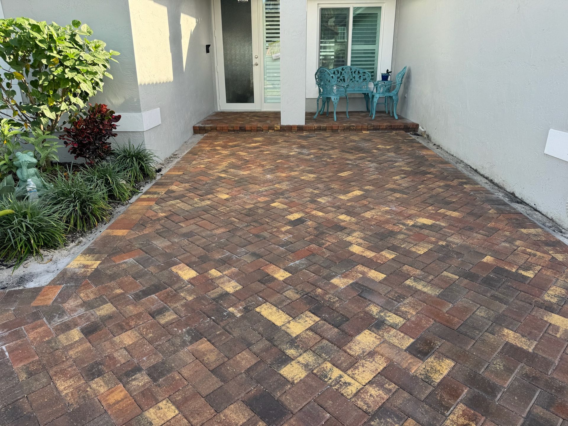 A brick driveway with a bench and chairs in front of a house.