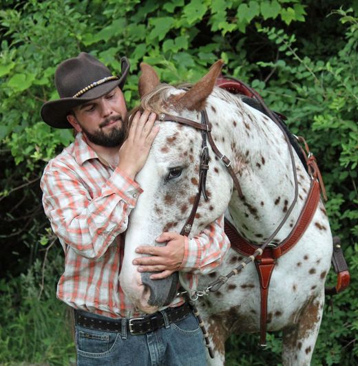 A man in a cowboy hat is petting a spotted horse