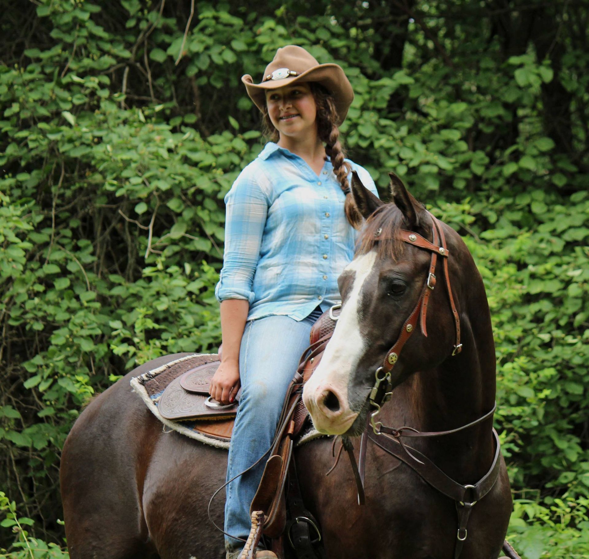 A woman in a cowboy hat is riding a brown horse