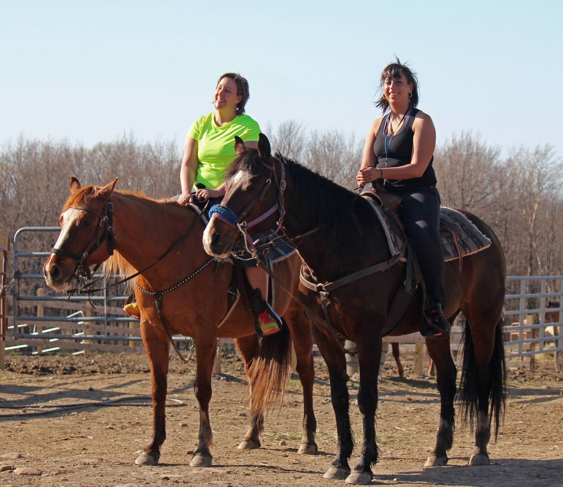 Two women are riding horses in a dirt field