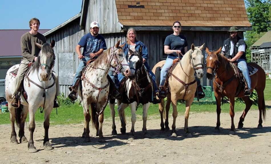 A group of people riding horses in front of a barn