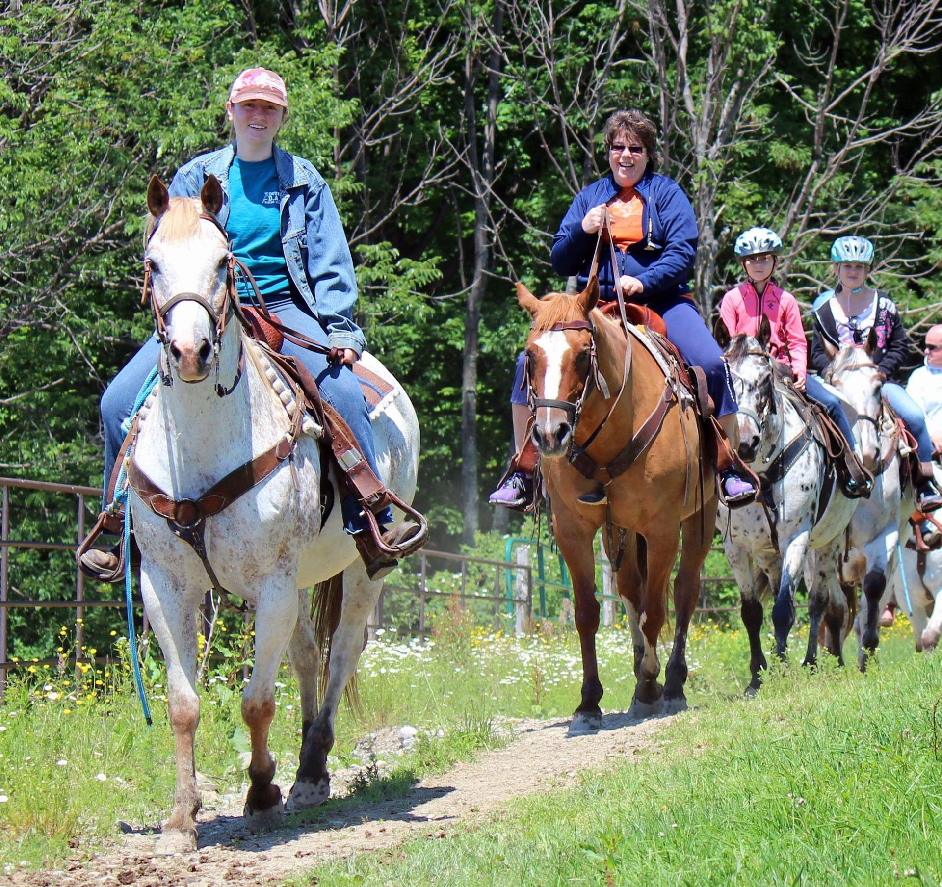 A group of people are riding horses down a dirt path