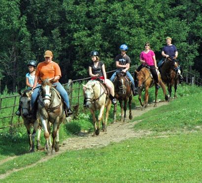 A group of people are riding horses down a dirt path